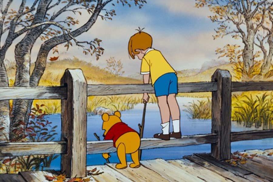 Winnie the Pooh (voiced by Sterling Holloway) and Christopher Robin play a game of Poohsticks together (Disney).