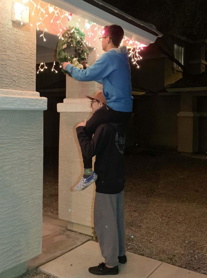 Seniors Bryce Harger and Ethan Le are hanging up a Christmas wreath. Le is on Hargers shoulders while hanging the wreath underneath a house entrance.