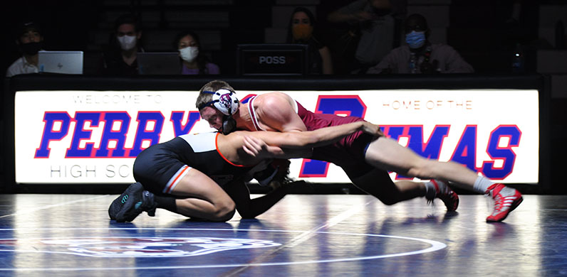Caleb+Milnes+is+wrestling+opposite+team+opponent+during+a+match.+Milnes+is+working+on+pinning+opponent+down.