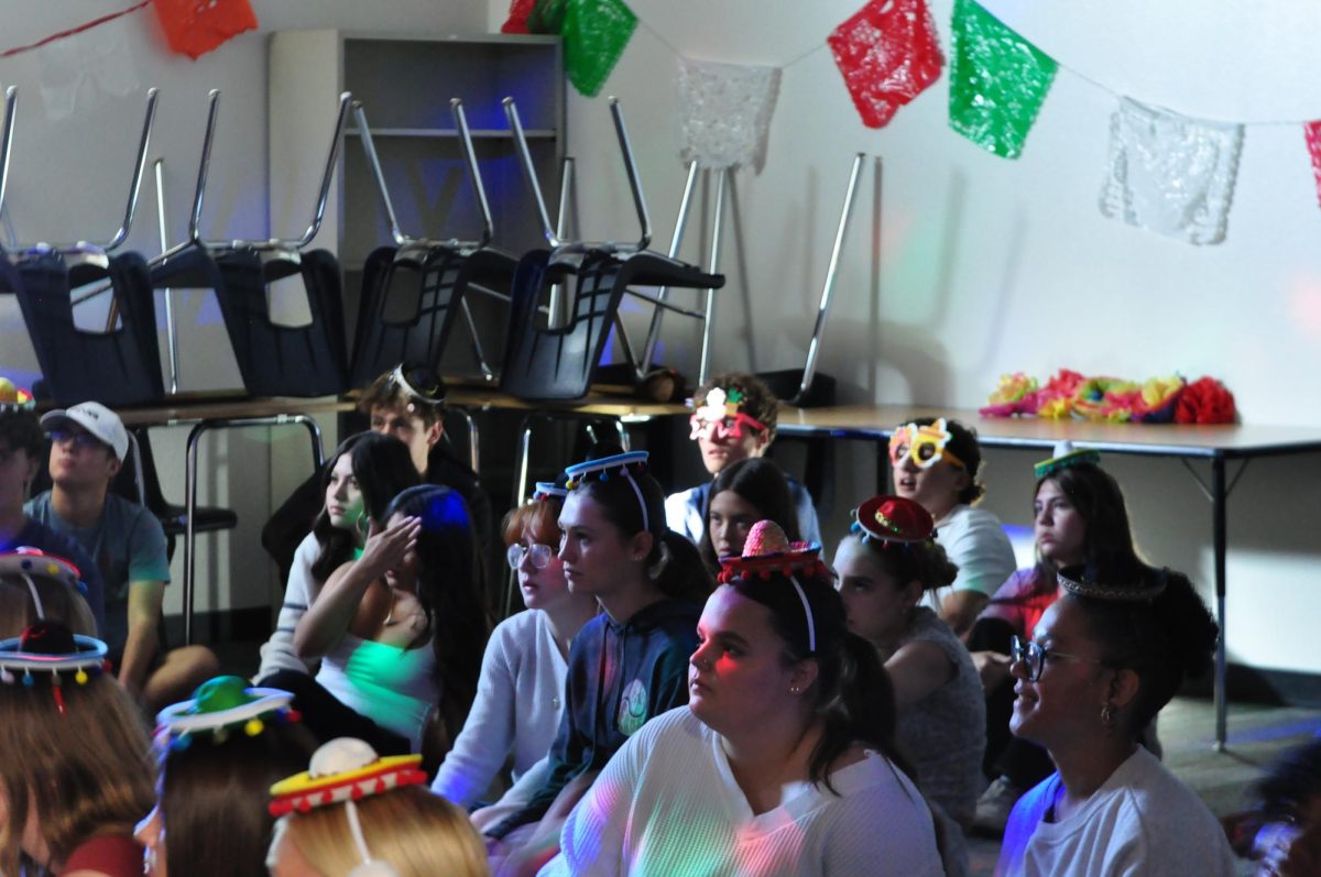 Students sit on the floor with different props to learn how to salsa.